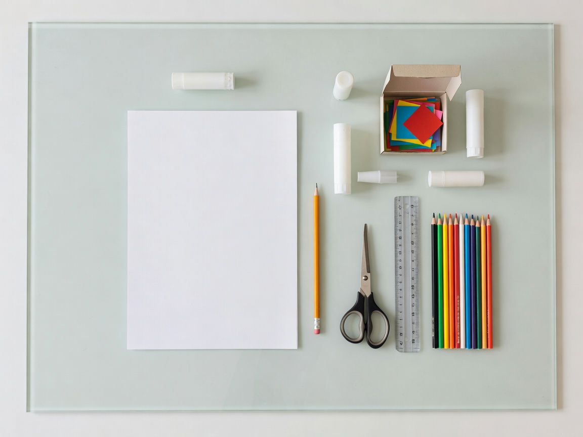 Straight-down reference photograph of paper, pencil and craft materials arranged within a clear tabletop boundary